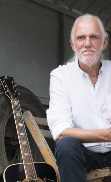 Dick van Altena in witte blouse naast gitaar staande afbeelding